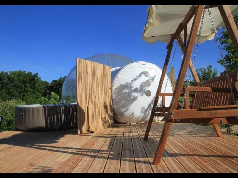 Hébergement insolite en bulle transparente avec terrasse en bois et balancelle.