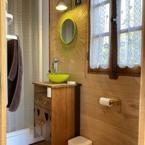 Salle de bain dun hébergement insolite en bois, avec un miroir coloré et des fenêtres lumineuses.