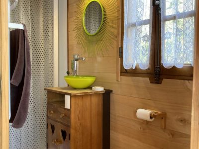 Salle de bain dun hébergement insolite en bois, avec un miroir coloré et des fenêtres lumineuses.