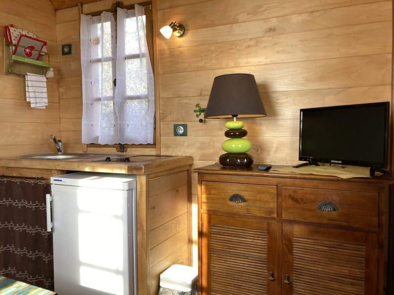 Cabane en bois cosy avec cuisine équipée et lampe colorée.