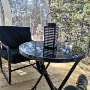 Hébergement insolite en bulle, table noire et lanterne dans un cadre naturel.
