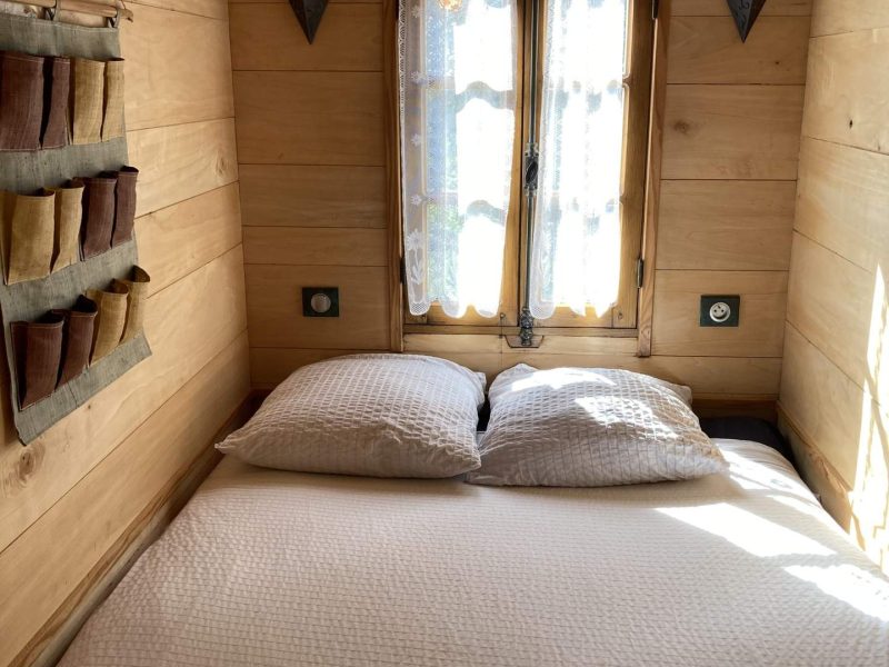 Chambre cosy en bois avec lit double et lumière naturelle à travers les fenêtres.