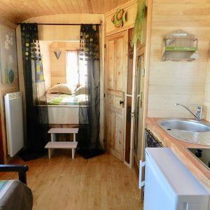 Hébergement insolite en roulotte, intérieur en bois chaleureux avec kitchenette.