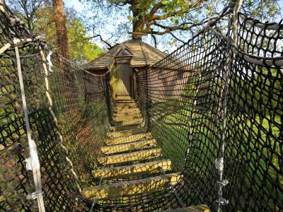 Cabane perchée en Bretagne, accessible par un pont en filet, entourée de verdure.