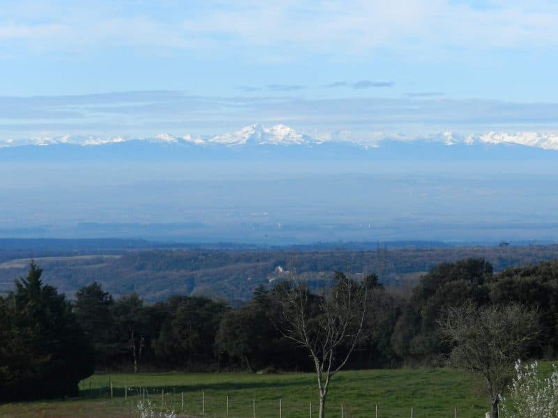 Vue panoramique depuis un gîte rural, avec les montagnes enneigées en arrière-plan.