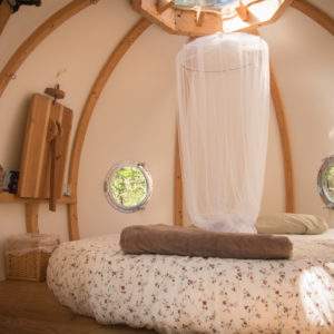 Hébergement insolite en Bretagne : cabane ronde avec lit douillet et fenêtres arrondies.