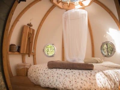 Hébergement insolite en Bretagne : cabane ronde avec lit douillet et fenêtres arrondies.