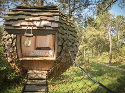 Cabane en bois ronde suspendue, entourée de verdure en Bretagne.