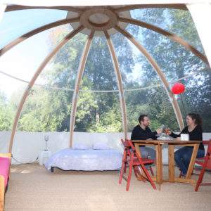 Dôme en bois transparent avec lit et table, idéal pour un séjour insolite en nature.