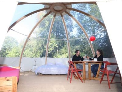 Dôme en bois transparent avec lit et table, idéal pour un séjour insolite en nature.