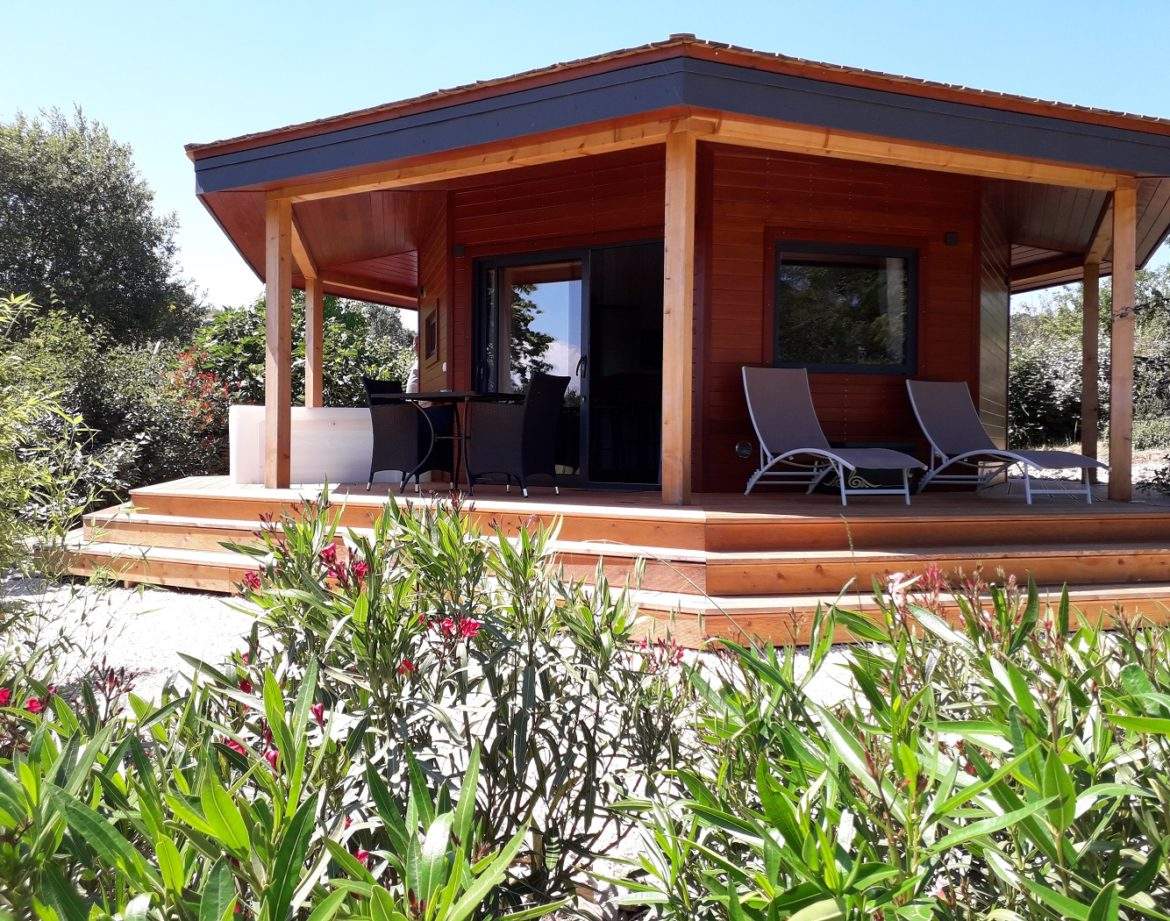 Cabane en bois à Languedoc-Roussillon, entourée de verdure et de fleurs colorées.