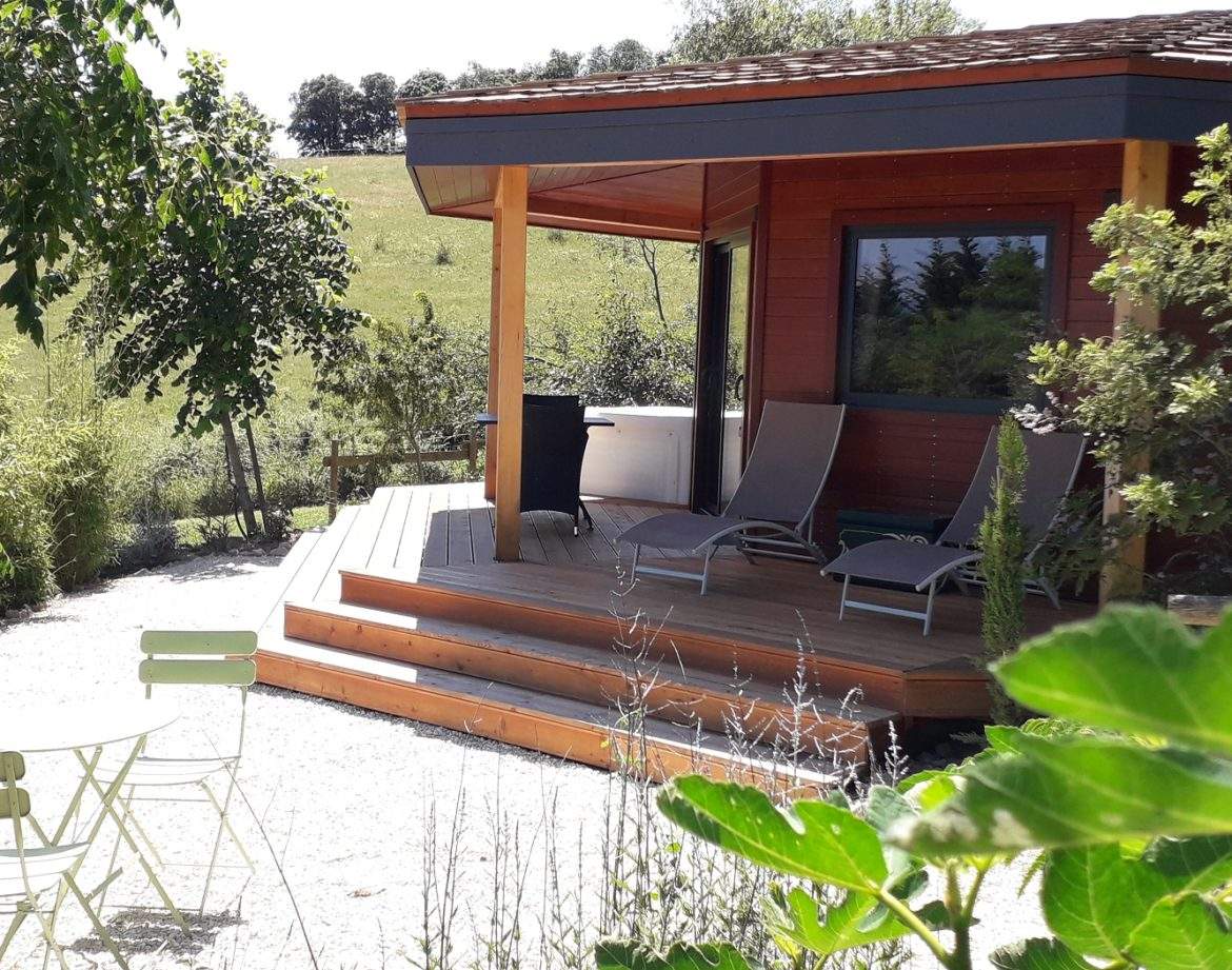 Chalet en bois avec terrasse ensoleillée, entouré de verdure apaisante.