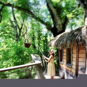 Cabane perchée dans les arbres, entourée de verdure, avec une petite fille et un panier.