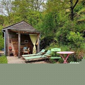 Cabane en bois avec jacuzzi, entourée de verdure et chaises longues confortables.