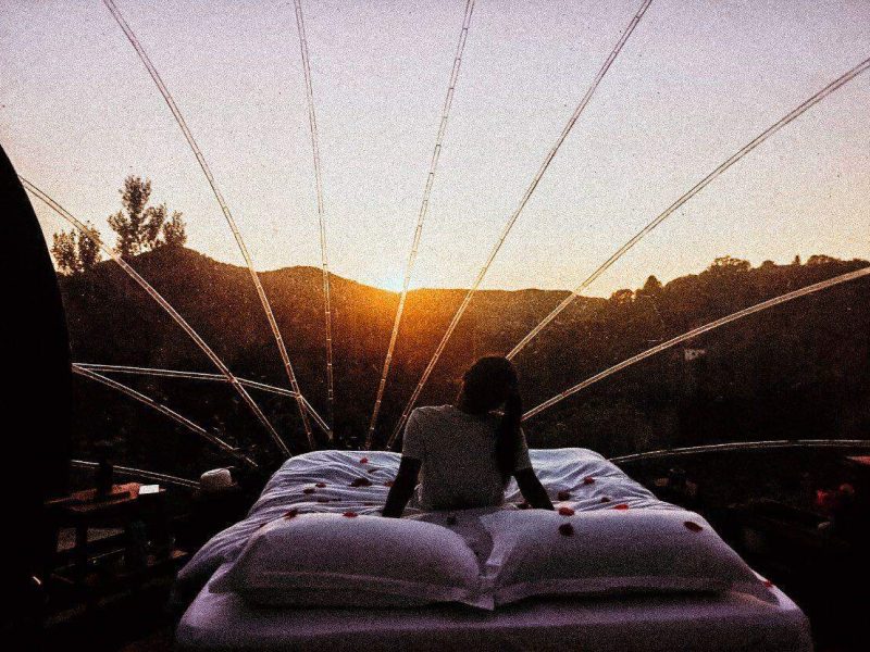 Dôme transparent avec vue sur le coucher de soleil, lit confortable et ambiance romantique.