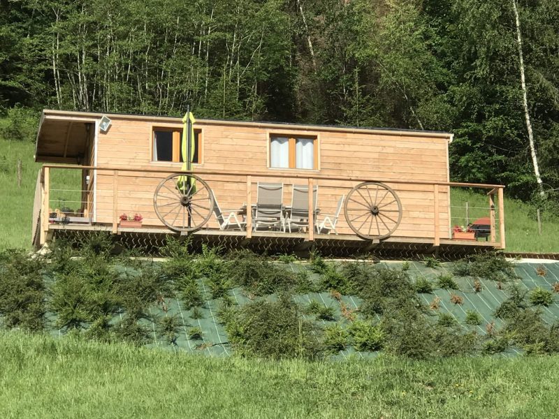 Cabane en bois avec terrasse, décorée de roues de chariot, au cœur de la nature.