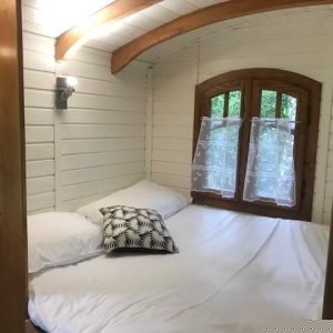 Chalet en bois cosy avec lit double et fenêtre en bois, ambiance chaleureuse.