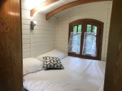 Chalet en bois cosy avec lit double et fenêtre en bois, ambiance chaleureuse.