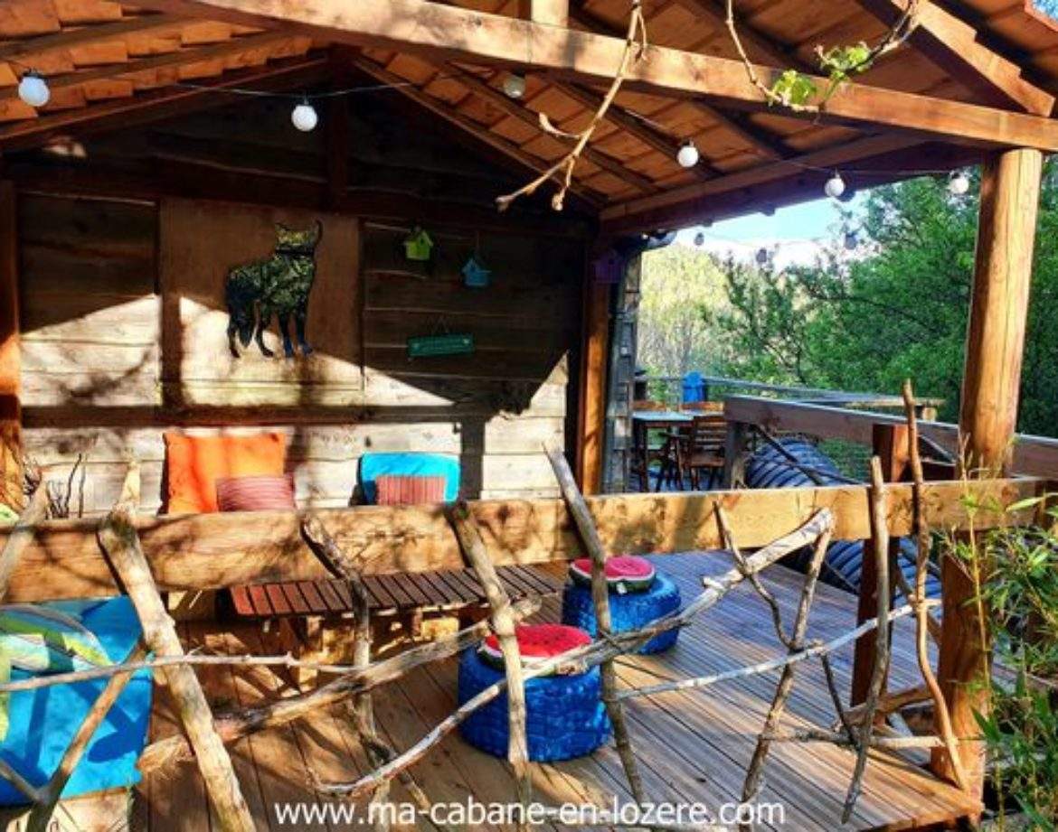 Cabane perchée en bois avec coussins colorés et éclairage doux dans la nature.