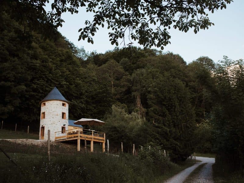 Charmante tour en pierre, entourée de verdure, avec terrasse en bois accueillante.