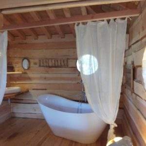 Cabane en bois avec baignoire design et fenêtres rondes, ambiance chaleureuse.
