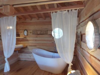Cabane en bois avec baignoire design et fenêtres rondes, ambiance chaleureuse.