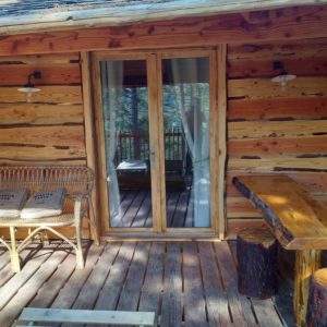 Cabane en bois avec terrasse, banc en osier et table en rondins, Auvergne-Rhône-Alpes.