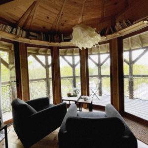 Cabane en bois avec vue panoramique, fauteuils confortables et lumière naturelle.