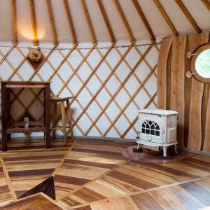 Yourte en Bourgogne, intérieur en bois chaleureux avec un poêle vintage et une fenêtre ronde.