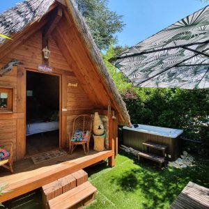 Cabane en bois avec jacuzzi, entourée de verdure et dun parasol à motifs.