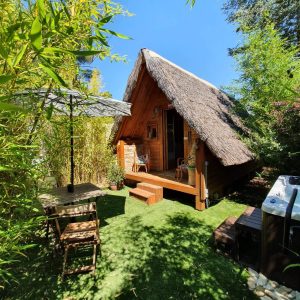 Cabane en bois avec toit de chaume, entourée de bambous et jacuzzi.
