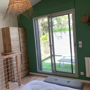 Chambre moderne en hébergement insolite, avec mur vert et grande fenêtre donnant sur le jardin.