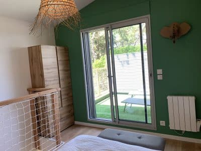 Chambre moderne en hébergement insolite, avec mur vert et grande fenêtre donnant sur le jardin.