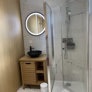 Salle de bain moderne dun hébergement insolite en Aquitaine, avec douche vitrée et miroir rond.
