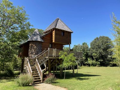 Cabane perchée en bois avec toit en ardoise, entourée de verdure en Aquitaine.