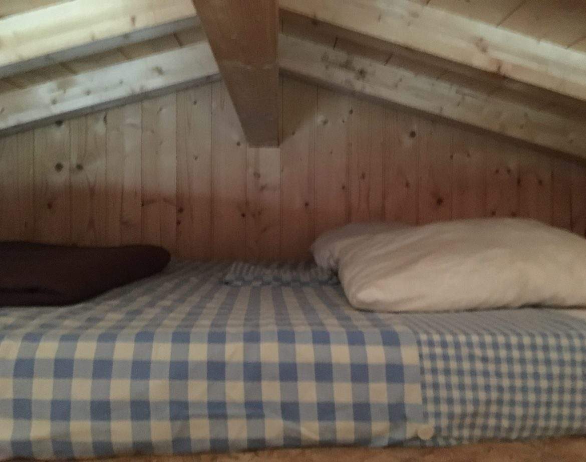 Chambre en mezzanine en bois avec lit à carreaux, ambiance cosy et chaleureuse.