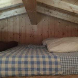 Chambre en mezzanine en bois avec lit à carreaux, ambiance cosy et chaleureuse.