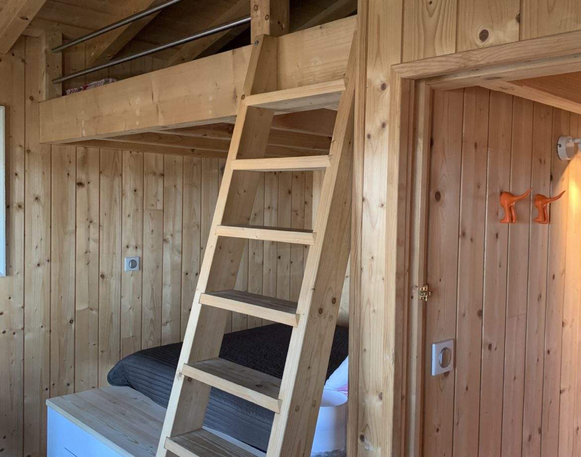 Cabane en bois avec mezzanine et échelle, ambiance chaleureuse et naturelle.