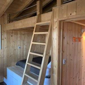 Cabane en bois avec mezzanine et échelle, ambiance chaleureuse et naturelle.