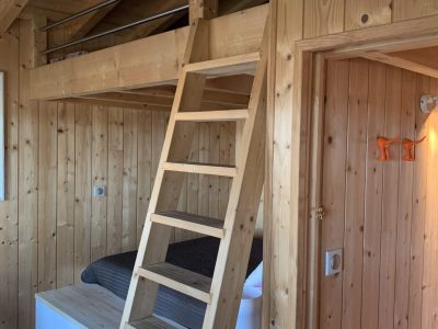 Cabane en bois avec mezzanine et échelle, ambiance chaleureuse et naturelle.