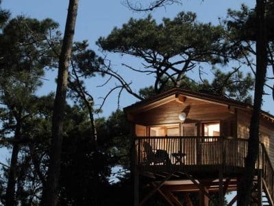 Cabane perchée en bois dans les arbres, éclairée par une douce lumière.