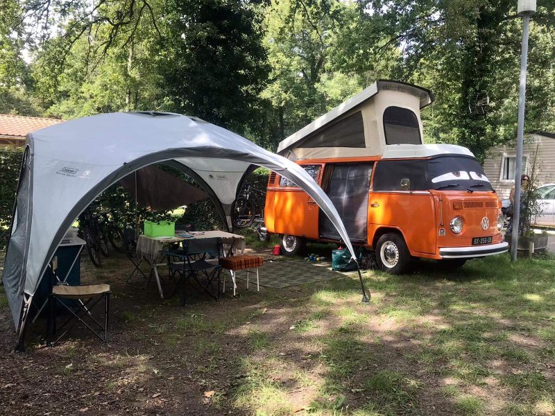 Camping-car vintage orange sous un auvent, entouré dun cadre verdoyant.