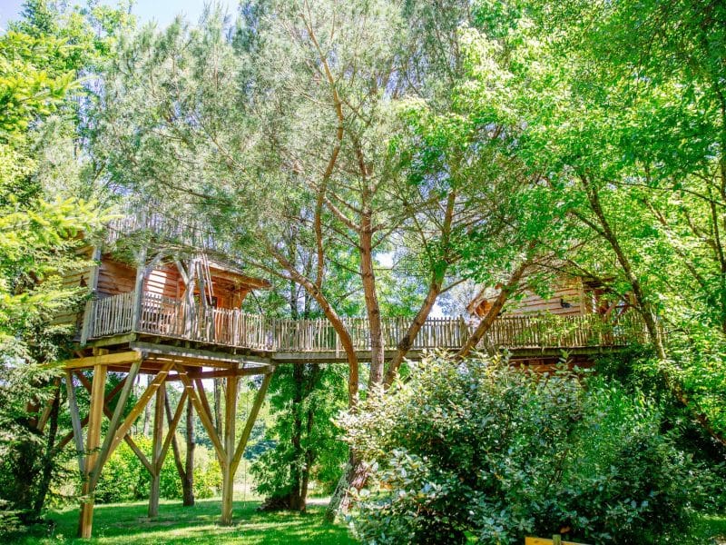 Cabane perchée dans les arbres, entourée de verdure luxuriante en Aquitaine.