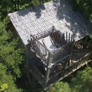 Cabane perchée en bois, entourée darbres, avec une terrasse ensoleillée.