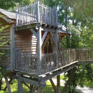 Cabane perchée en bois avec terrasse, entourée darbres verdoyants en Aquitaine.