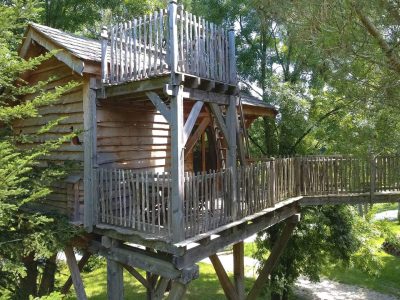 Cabane perchée en bois avec terrasse, entourée darbres verdoyants en Aquitaine.