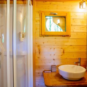 Cabane en bois avec salle de bain moderne et fenêtre sur la nature.