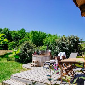 Hébergement insolite en Aquitaine : chalet en bois avec jacuzzi sur une terrasse ensoleillée.