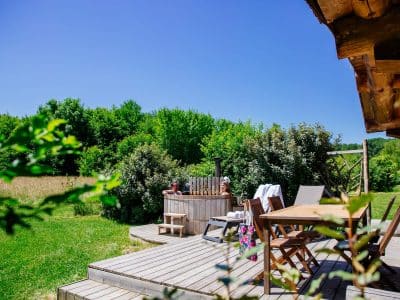 Hébergement insolite en Aquitaine : chalet en bois avec jacuzzi sur une terrasse ensoleillée.