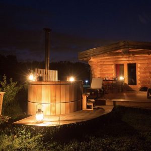 Cabane en bois avec un bain nordique, illuminée par des lanternes au crépuscule.